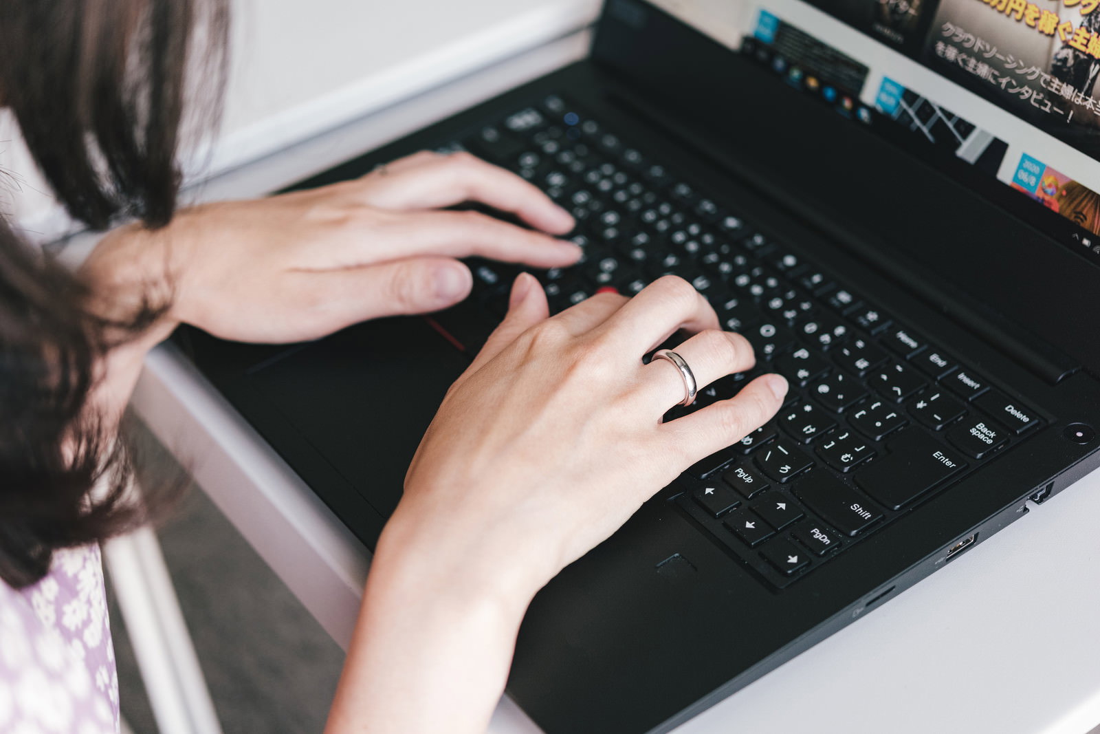 黒いノートパソコンのキーボードでタイピングする女性の手元