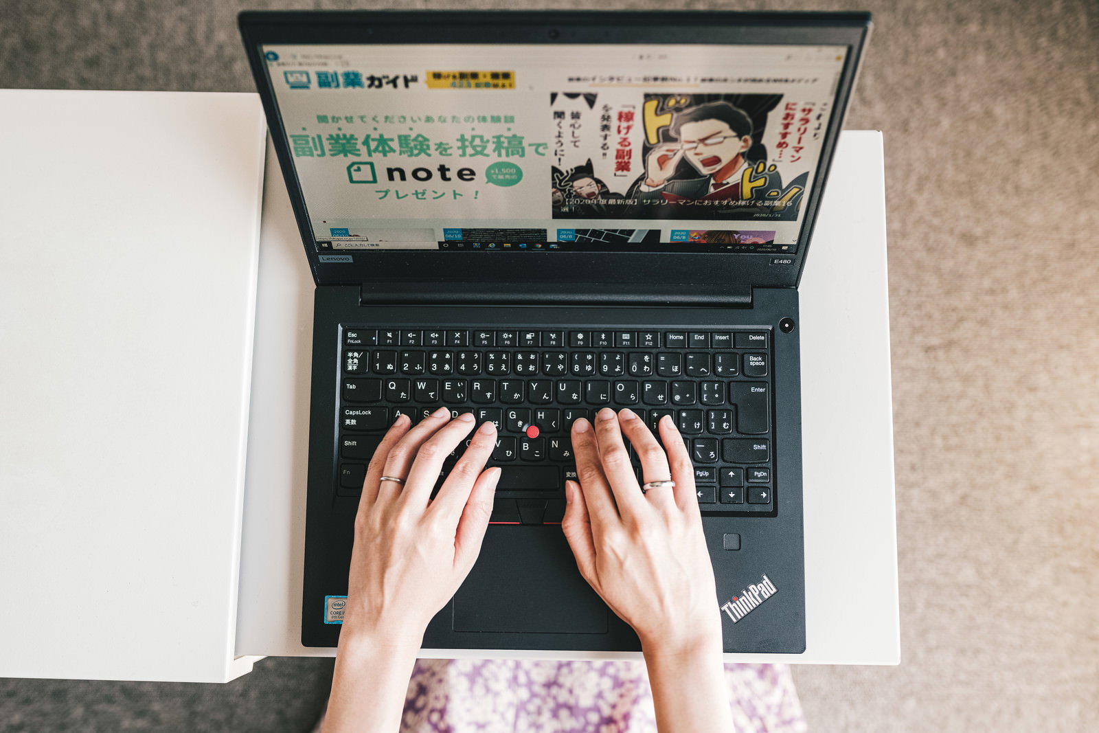 白い机の上でノートパソコンのキーボードをタイピングする女性の手元