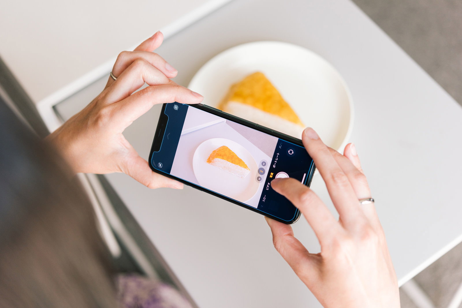 スマートフォンでお皿に盛られたチーズケーキを撮影している手元