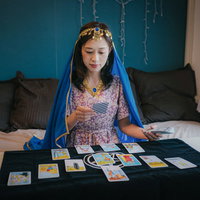 青い髪のタロット占い師が黒いテーブルでカードを並べる女性の写真