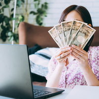 在宅ワークで得た報酬、一万円札を手に持つ女性の写真
