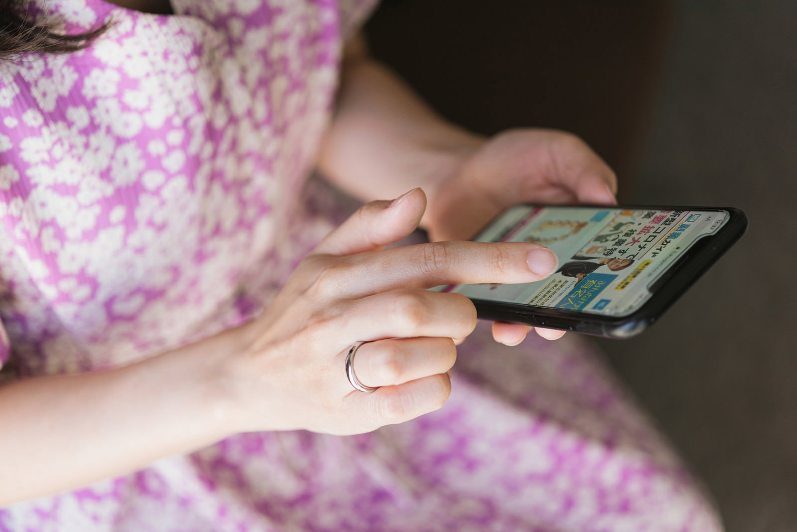 花柄の服を着た女性がスマートフォンを操作している手元のクローズアップ