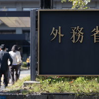 外務省の庁舎前を行き来する職員の後ろ姿と建物入口の写真