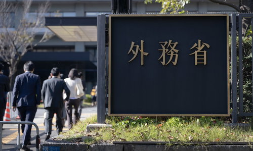 外務省の庁舎前を行き来する職員の後ろ姿と建物入口