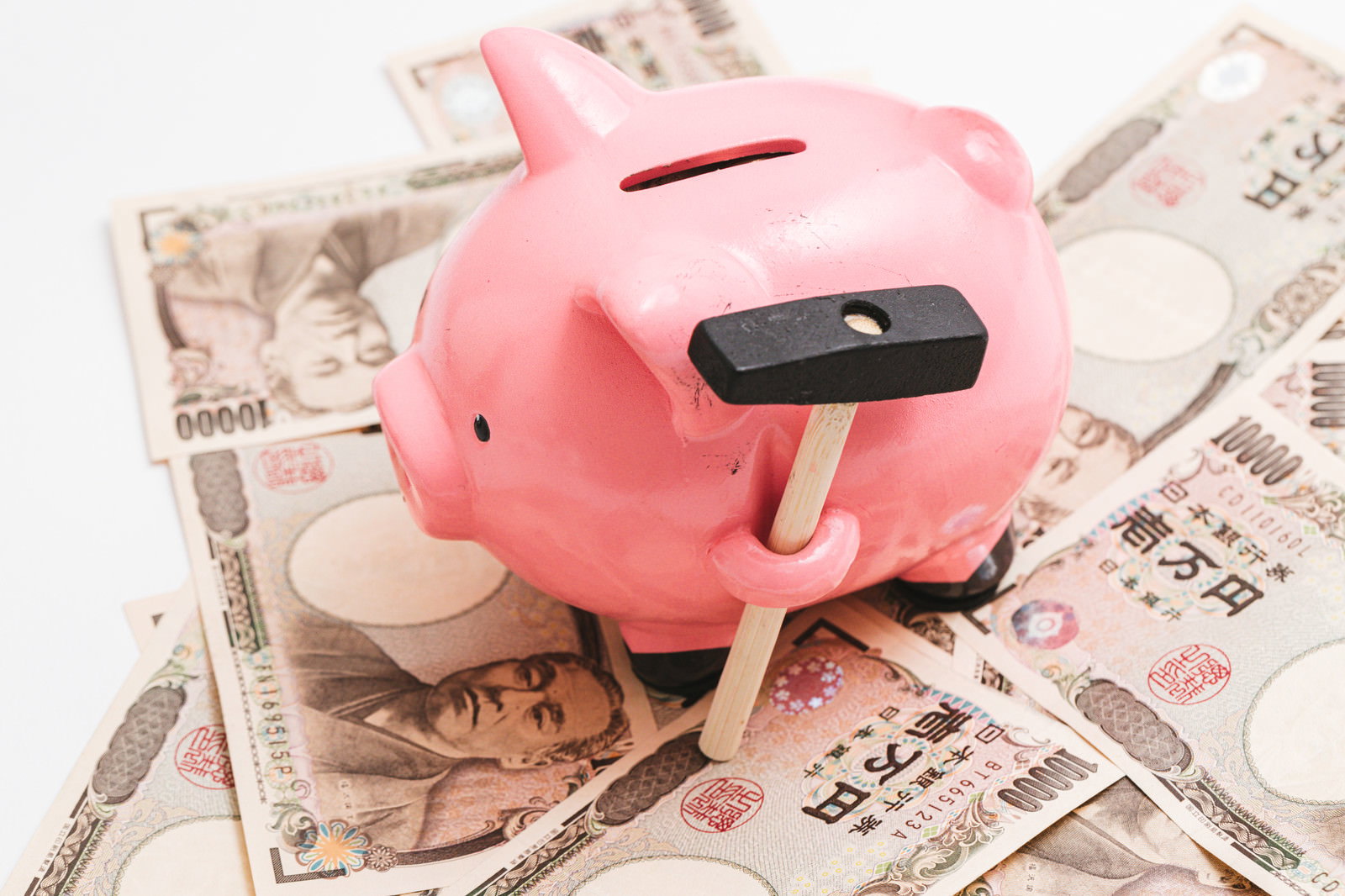 新聞紙の上に置かれたピンクの豚の貯金箱と散らばった一万円札