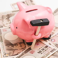 ピンクの豚の貯金箱と1万円札と新聞紙の家計管理の写真