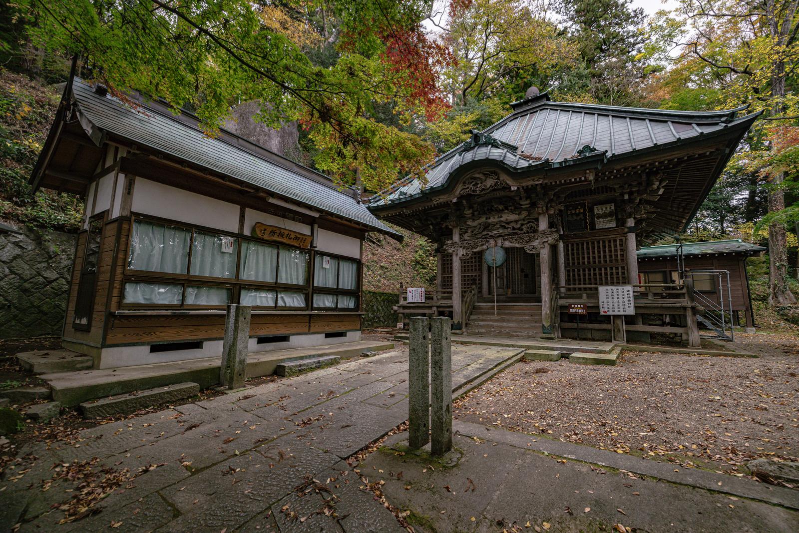 秋の紅葉に囲まれた岩角寺の毘沙門堂と御札授所の全景