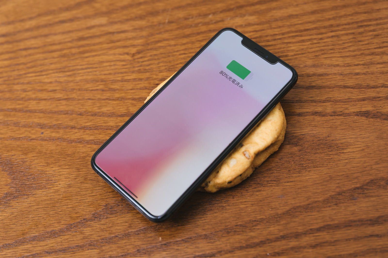 木目のテーブルの上でがんもどきの上にスマートフォンを置いてワイヤレス充電している様子