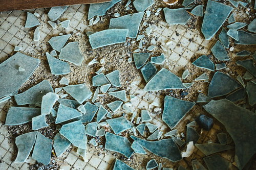 床に散乱するガラス片と剥がれたタイルの廃墟風景