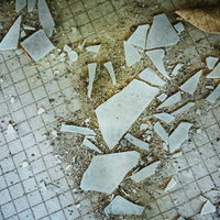 廃墟のタイル床に散乱するガラス片と破損した建物内部の状態の写真