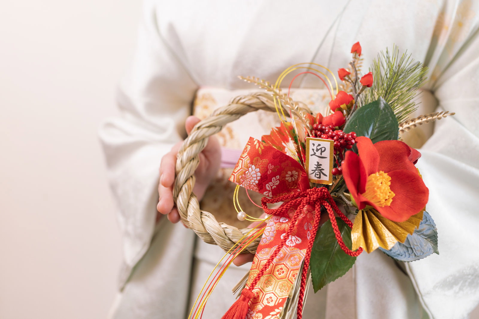 白い着物を着た女性が迎春の正月飾りを両手で持っている様子［モデル：yumiko］