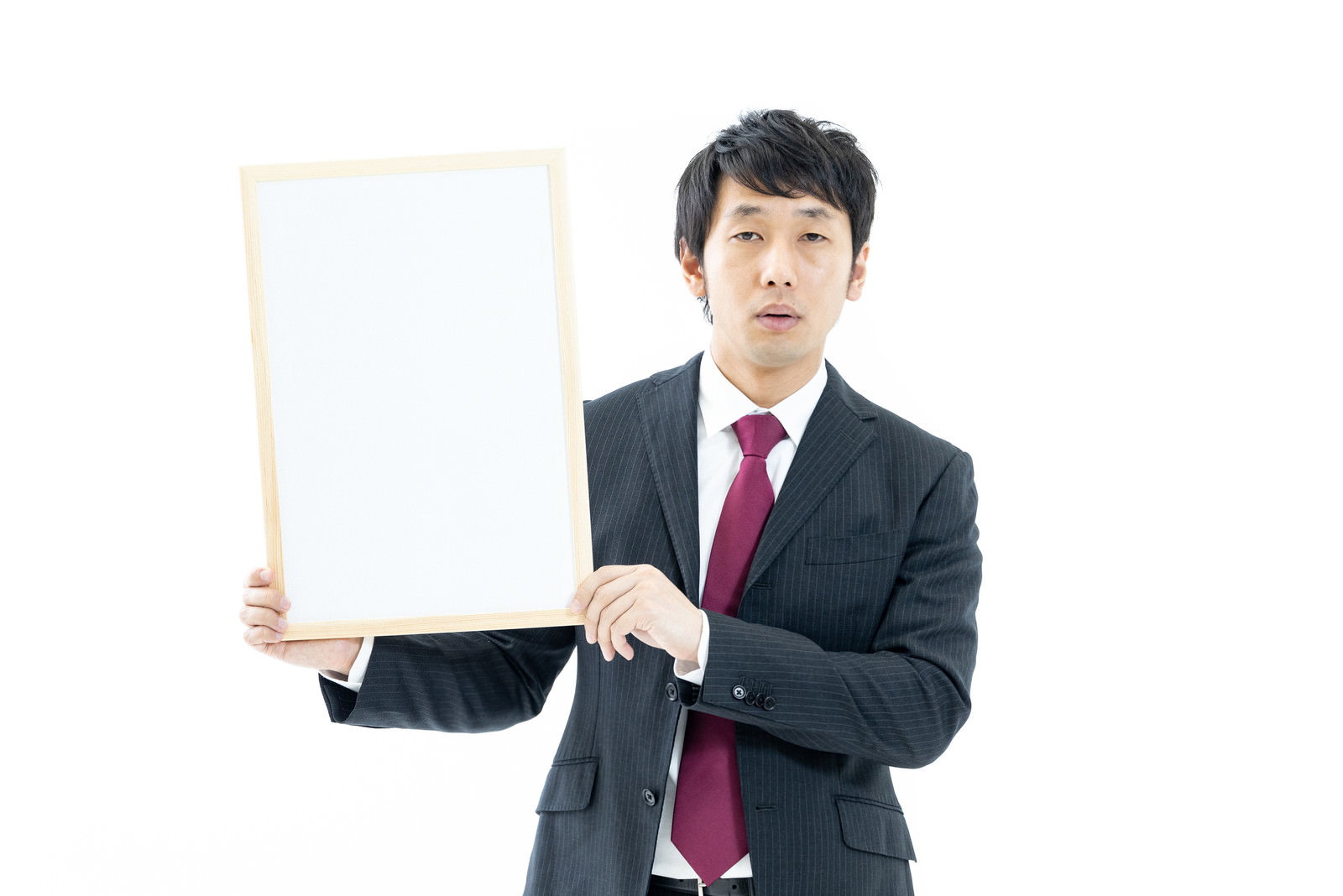 ホワイトボードを持つ紺色スーツの男性営業マン。深紅色のネクタイ、白いシャツ。白背景。［モデル：大川竜弥］