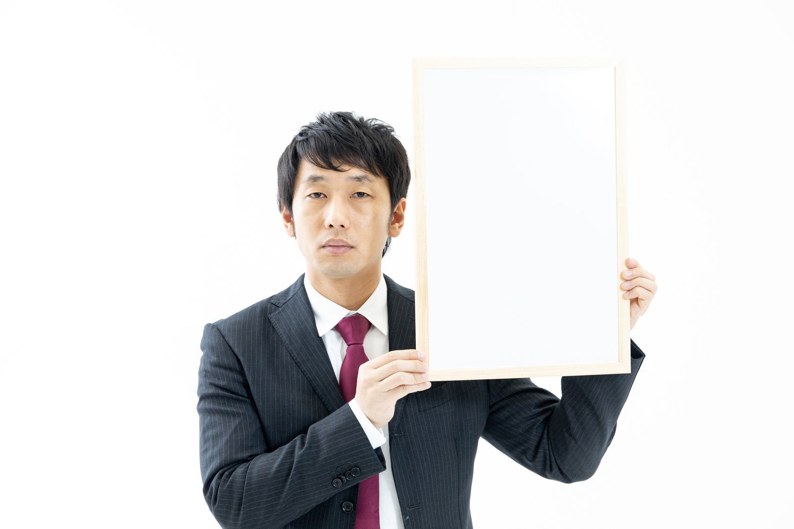 チベットスナギツネの顔マネをしながら白いボードを持つスーツ姿の男性［モデル：大川竜弥］