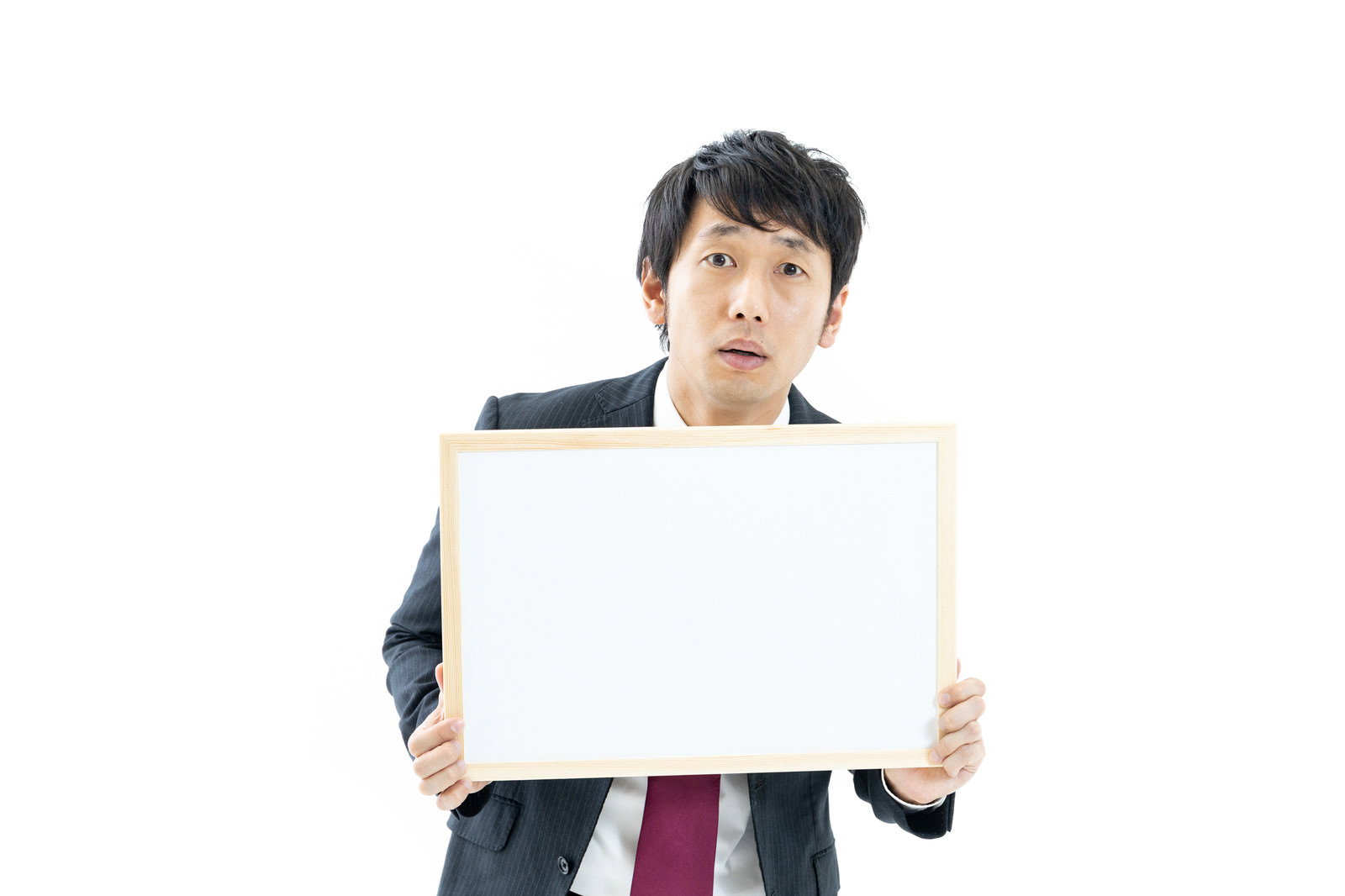白いホワイトボードを持って不安げな表情を見せるスーツ姿のディレクター男性［モデル：大川竜弥］