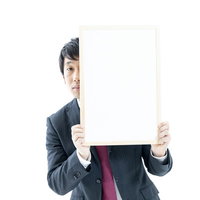 ホワイトボードからひょっこり顔を出すスーツ姿の男性の写真