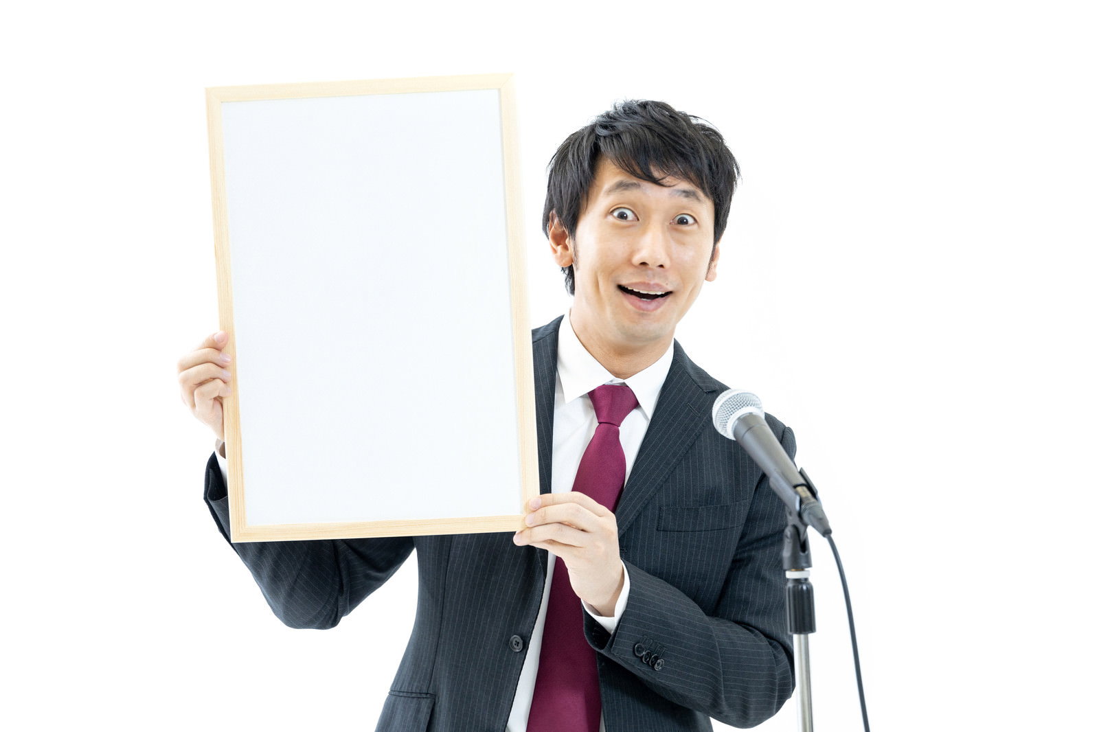 白いボードを持ちマイクで話すスーツ姿の男性［モデル：大川竜弥］