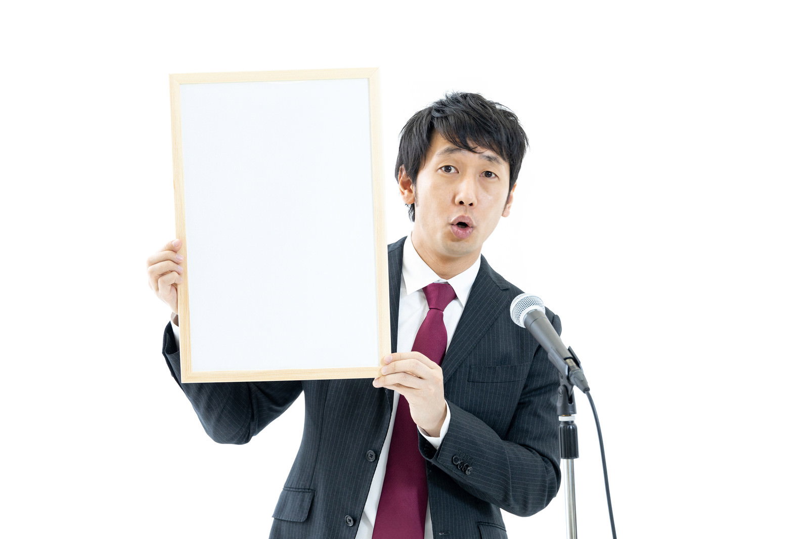白い紙とマイクを持つ赤いネクタイのスーツ姿の男性［モデル：大川竜弥］
