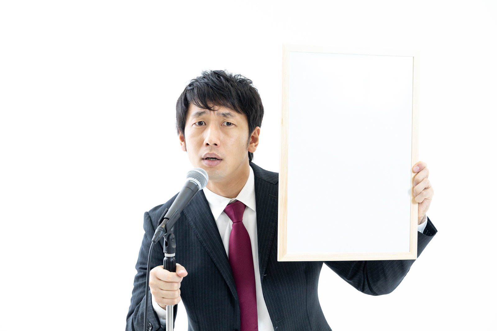 白いフリップを持って怒った表情を見せるスーツ姿の男性［モデル：大川竜弥］