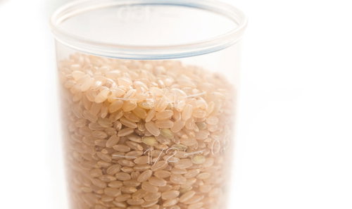 透明な計量カップに入った玄米の粒と計量風景