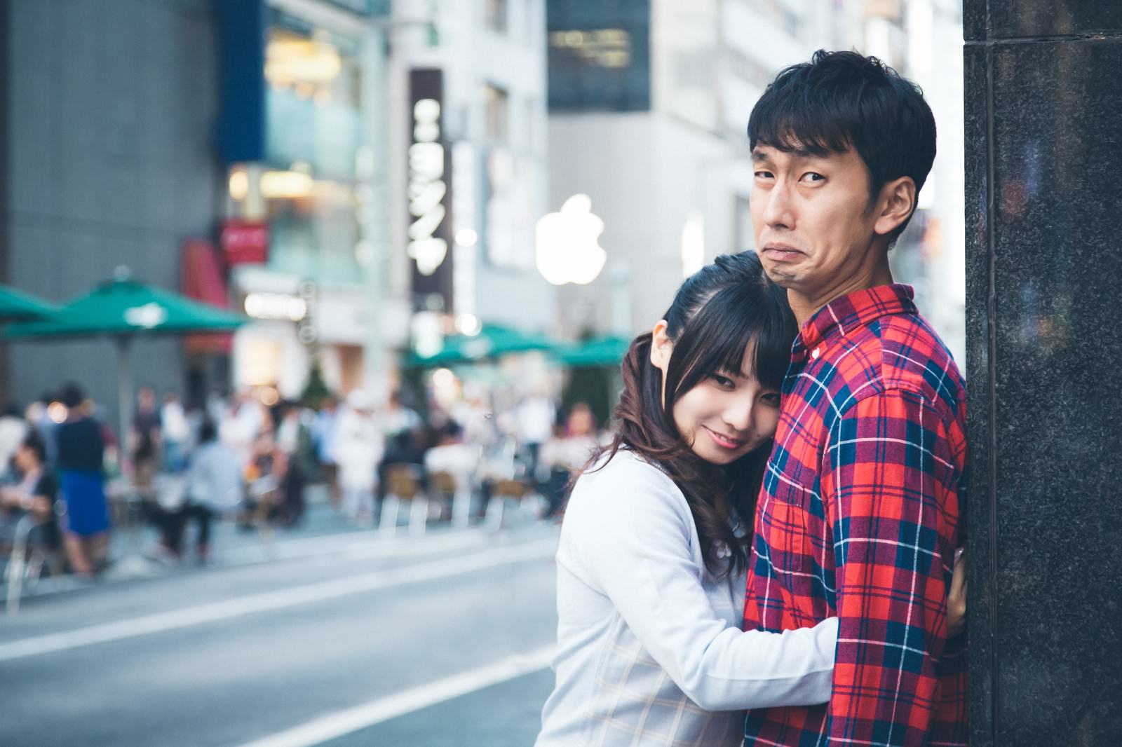 白いシャツの女性が赤チェックシャツの男性に壁ギュし、男性が困惑した表情を浮かべるカップル写真［モデル：大川竜弥 Lala］