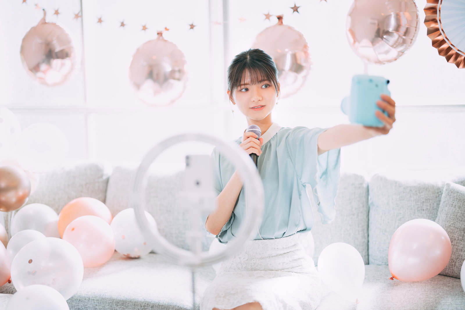パステルカラーの風船に囲まれた室内でスマートフォンを持って配信する女性［モデル：モデルリリース］