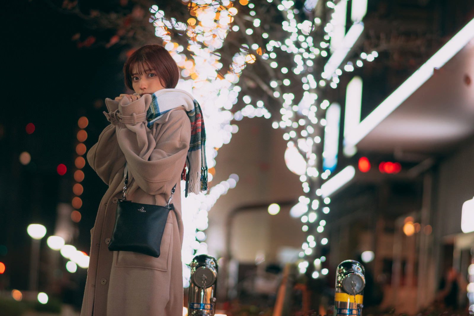 ライトアップされた駅前のイルミネーションの中でコートを着て待ち合わせしている女性［モデル：高尾実生］