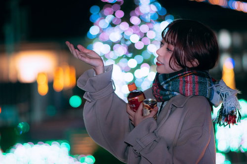 イルミネーションの玉ボケをバックに手を上げて喜ぶ彼女