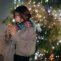 クリスマスイルミネーションの前で温かい飲み物を持ちながら待つ彼女の写真