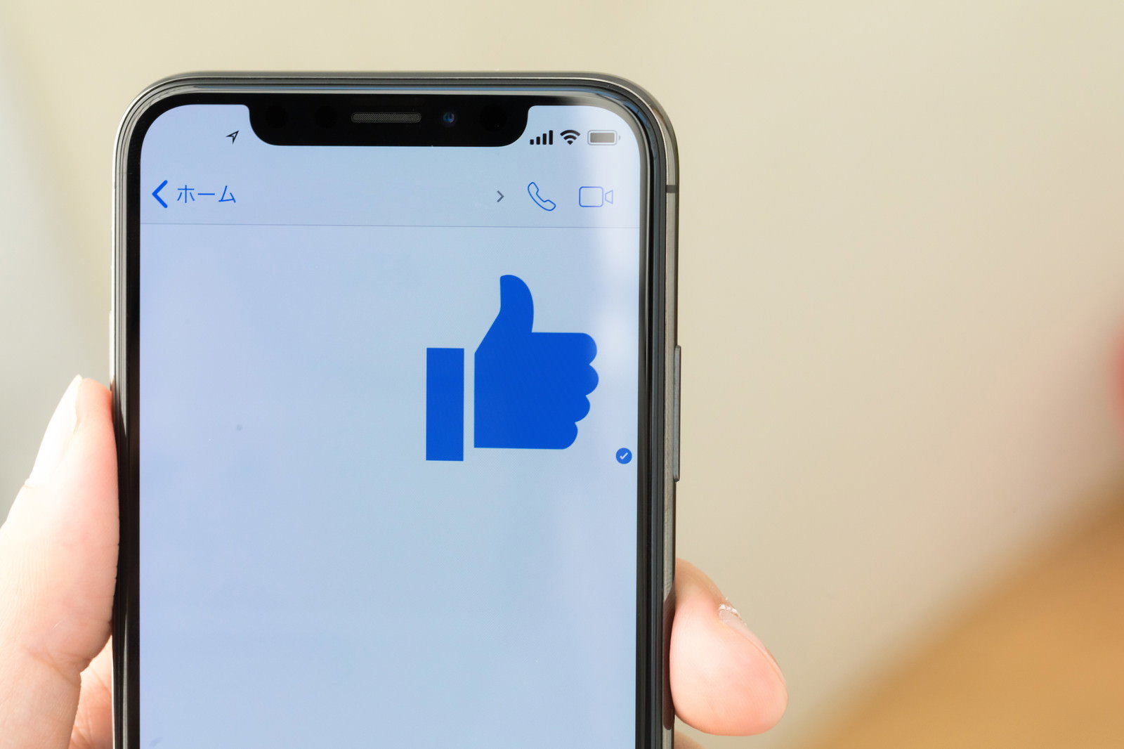 スマートフォンを持つ手とサムズアップアイコンが画面中央に表示されている