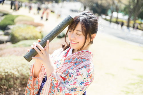 大学生活を思い返す卒業女子、花柄の着物と紫の袴で卒業証書を手に掲げた晴れ姿