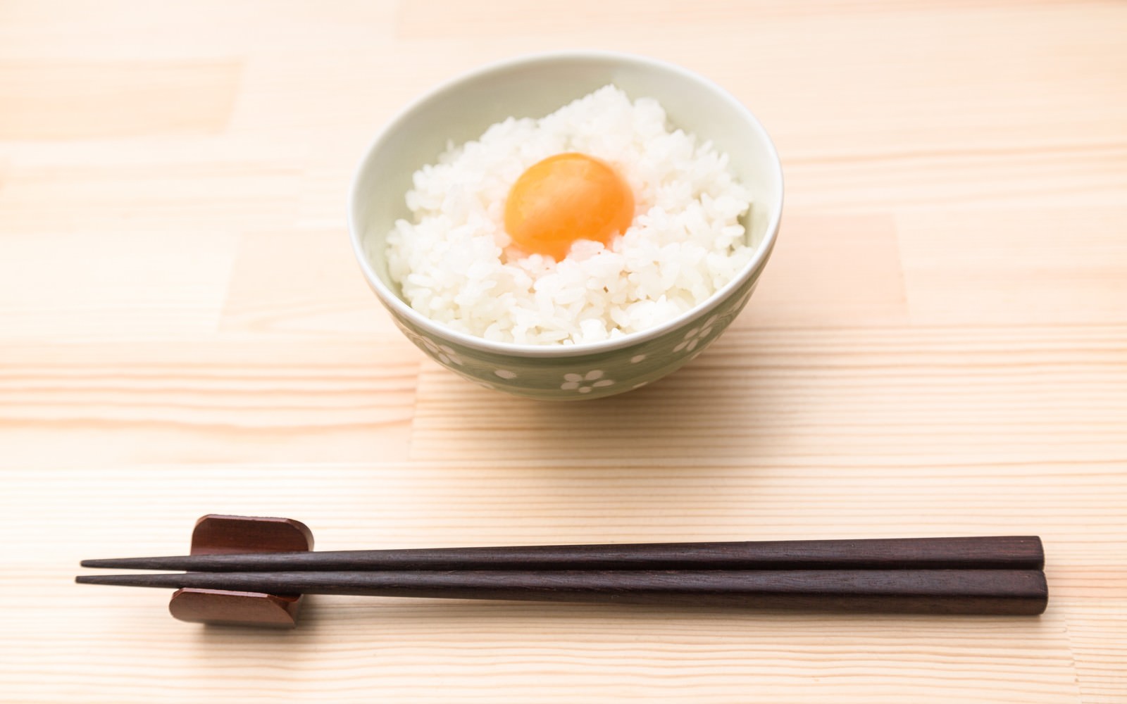 白い丼ぶりに盛られたご飯に生卵がのった卵かけごはんと黒い箸