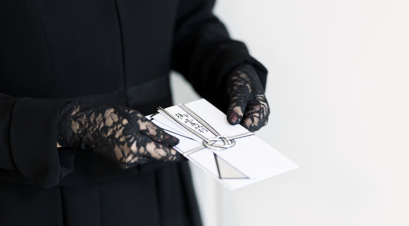 黒い服装の人が白い御霊前の不祝儀袋を手渡している様子