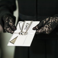 黒い手袋で持つ御霊前と書かれた不祝儀袋の香典袋の写真