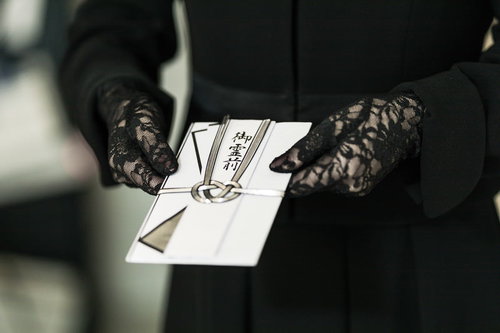 黒い手袋で持つ御霊前と書かれた不祝儀袋の香典袋