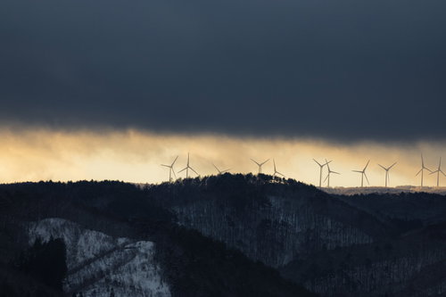 冬の山並みに立ち並ぶ風力発電の風車群と雪景色