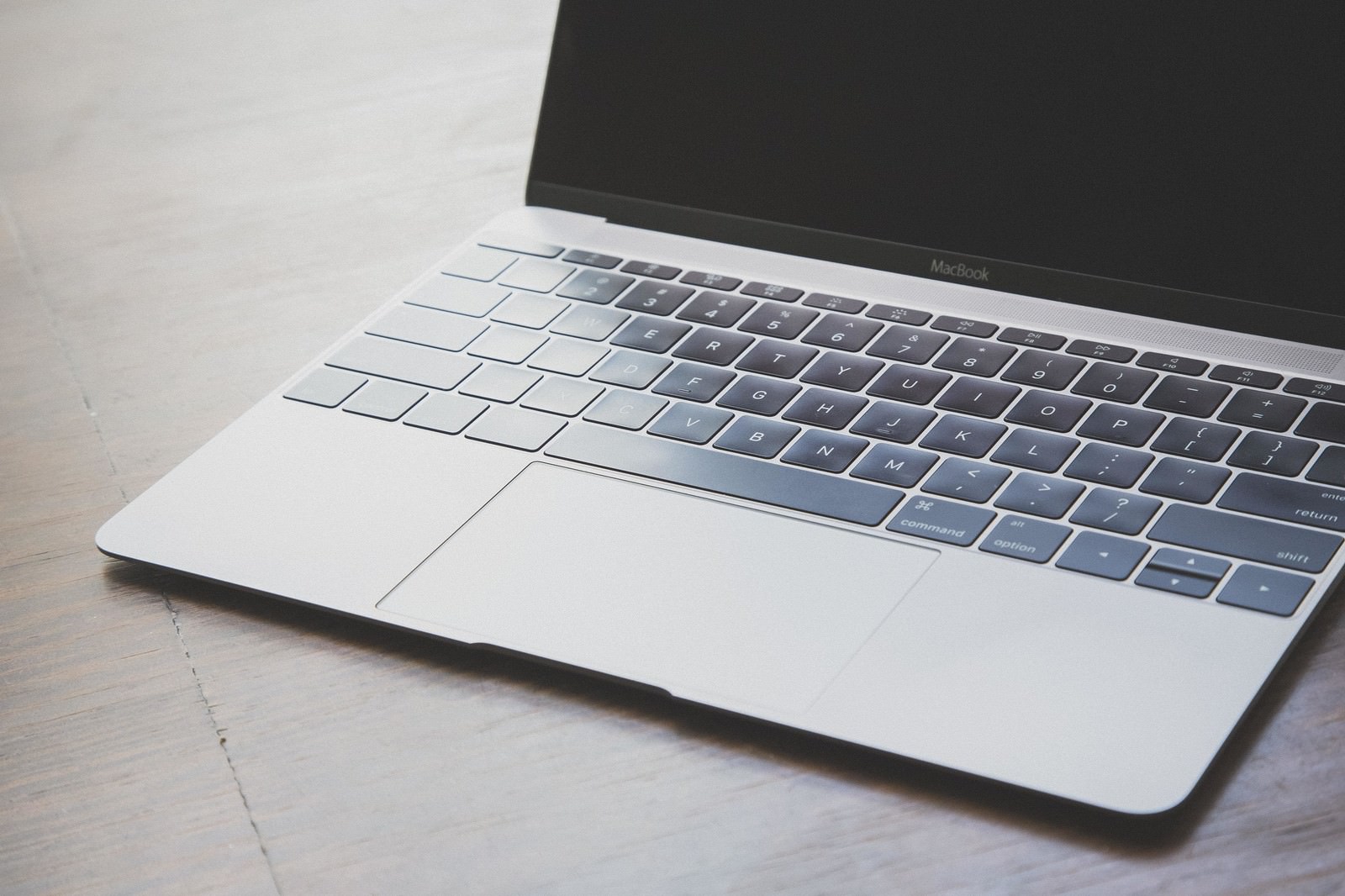 木目テーブルの上に置かれたMacBookのキーボードとディスプレイ