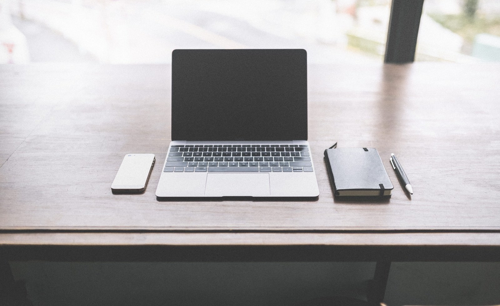 デスクにMacBookとスマホ、ノートが並んでいる