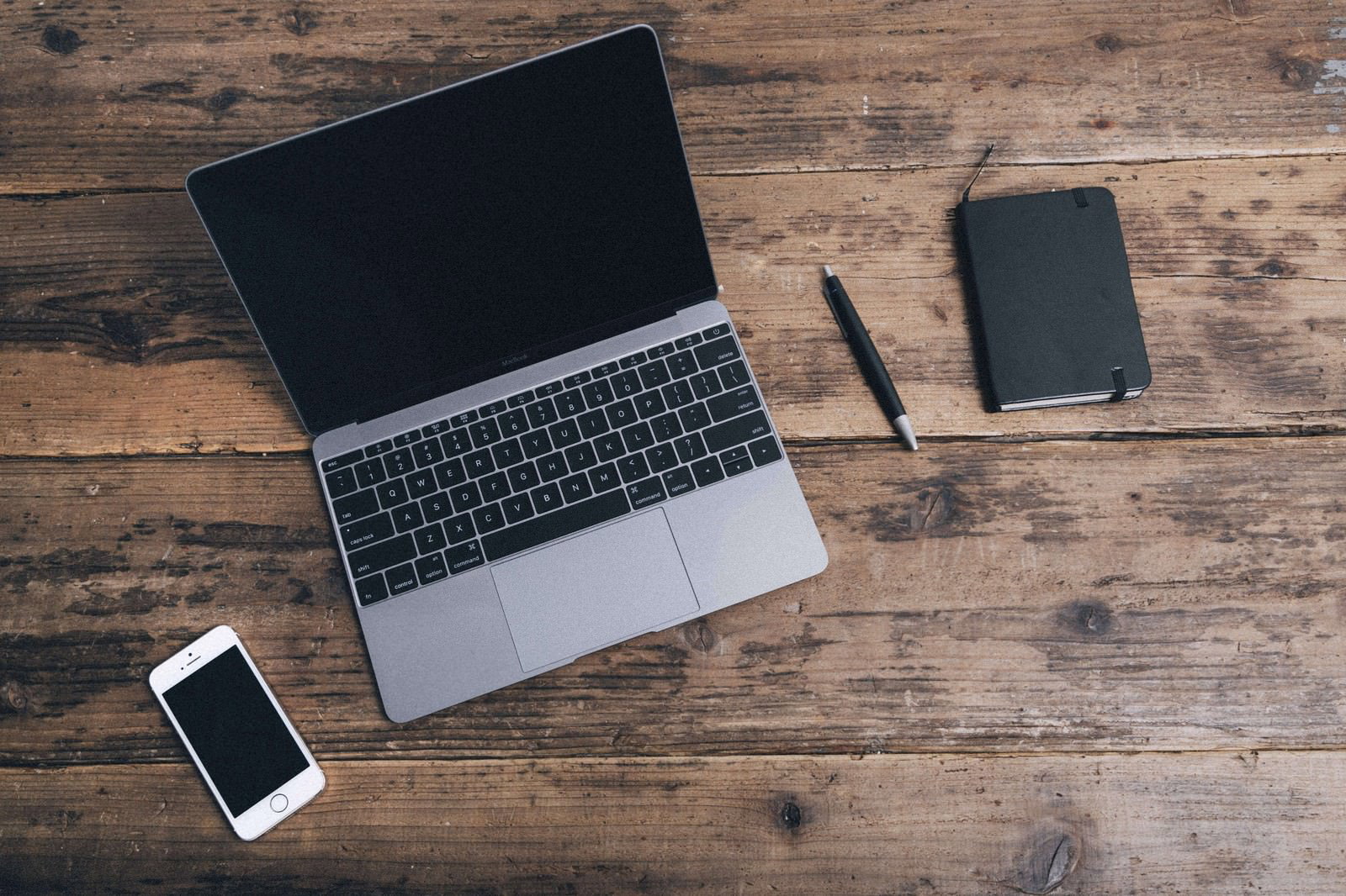 木製テーブルの上に置かれたMacBookとiPhoneとメモ帳