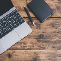 ノートパソコンと手帳のある木製デスクの写真