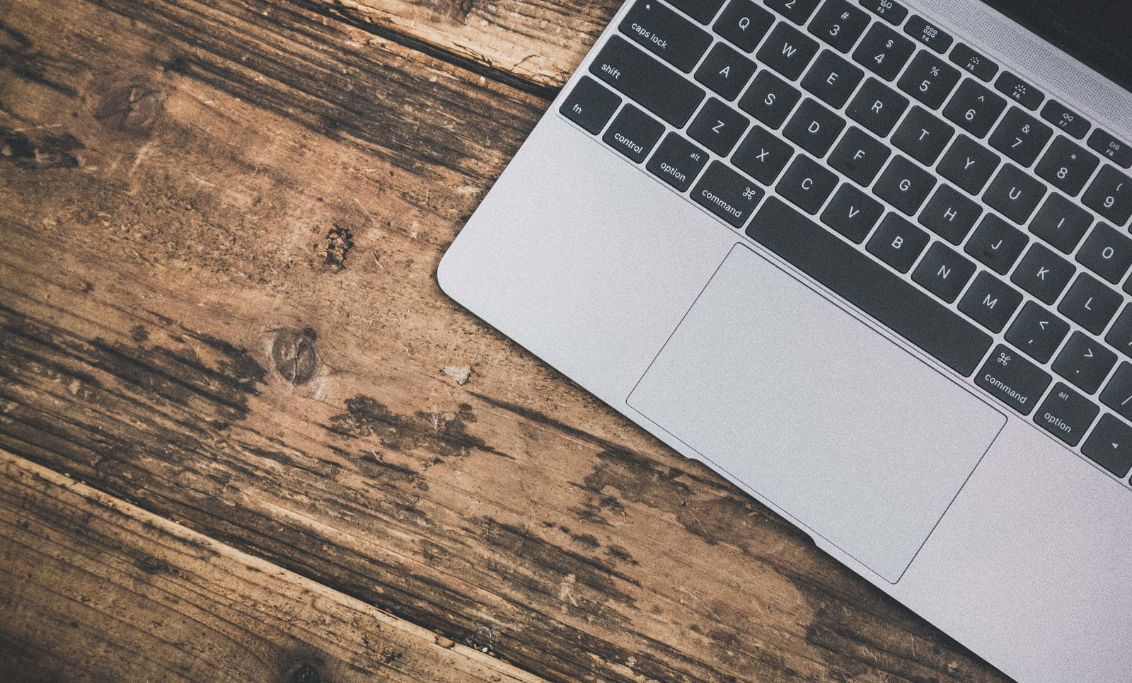 木目テーブルの上のMacBookのキーボードとトラックパッド