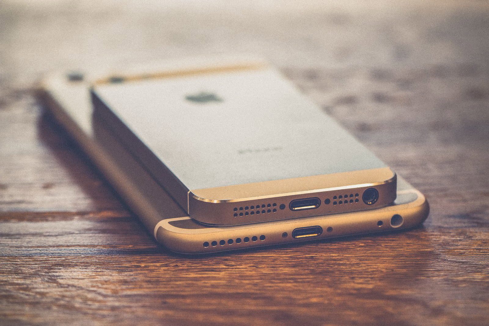 ゴールドのiPhone 2台を重ねて木目テーブルに置いてある