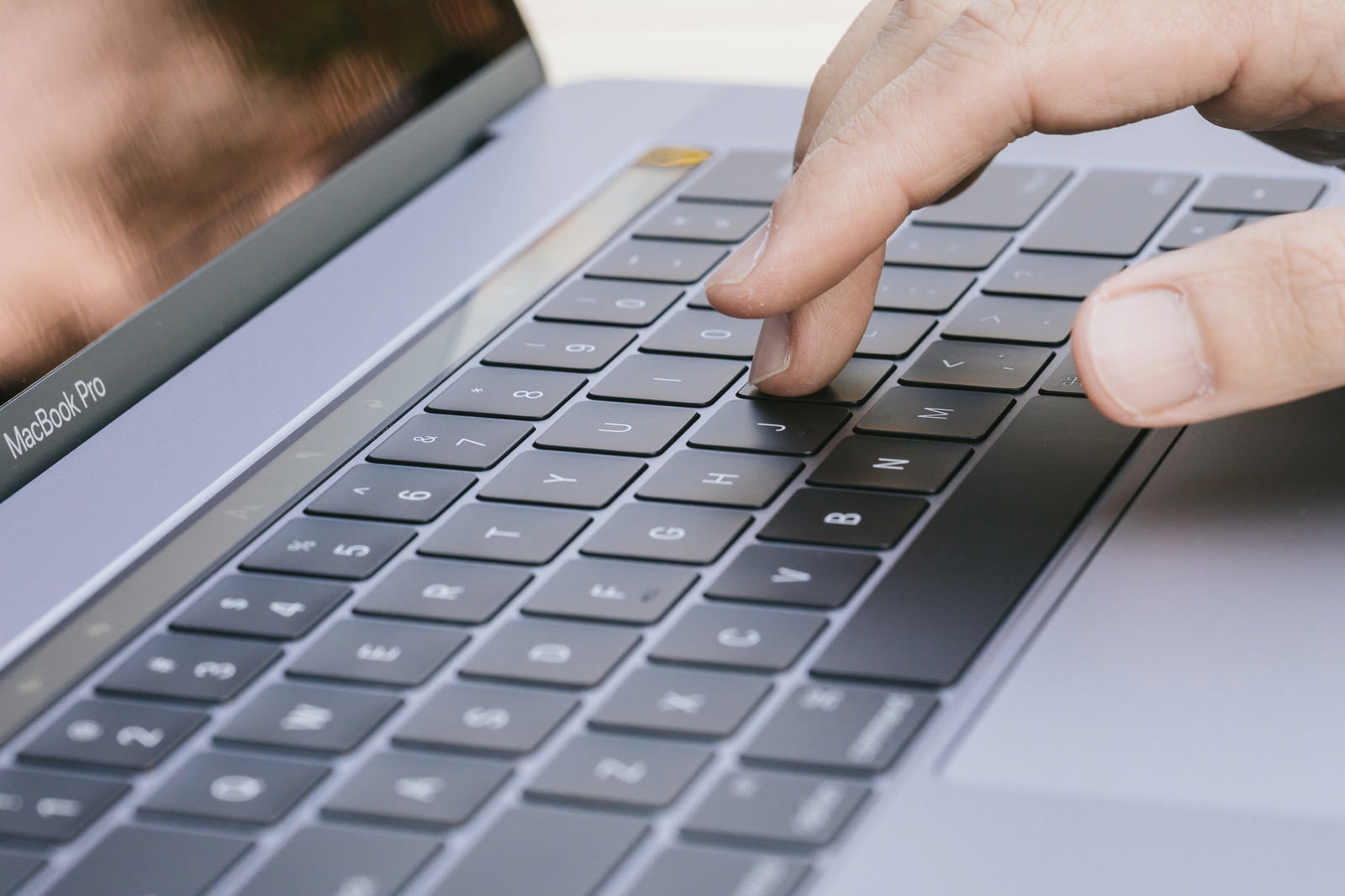 MacBook Proのキーボードを打つ手の指のクローズアップ