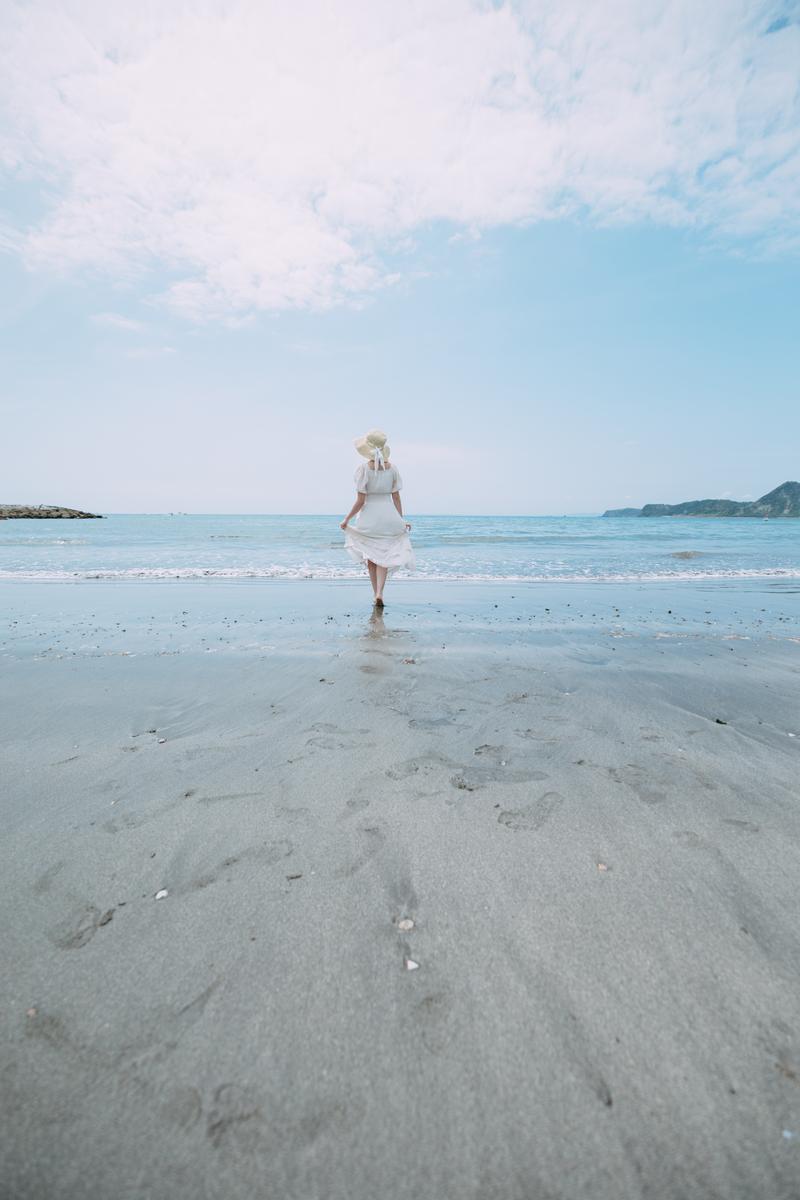 白いワンピース姿の女性が千葉県岩井海岸の波打ち際で立っている写真［モデル：茜さや］
