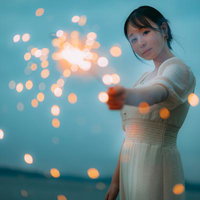 夜空に煌めく手持ち花火を楽しむ白いワンピースの女性の写真