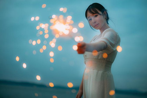 夜空に煌めく手持ち花火を楽しむ白いワンピースの女性