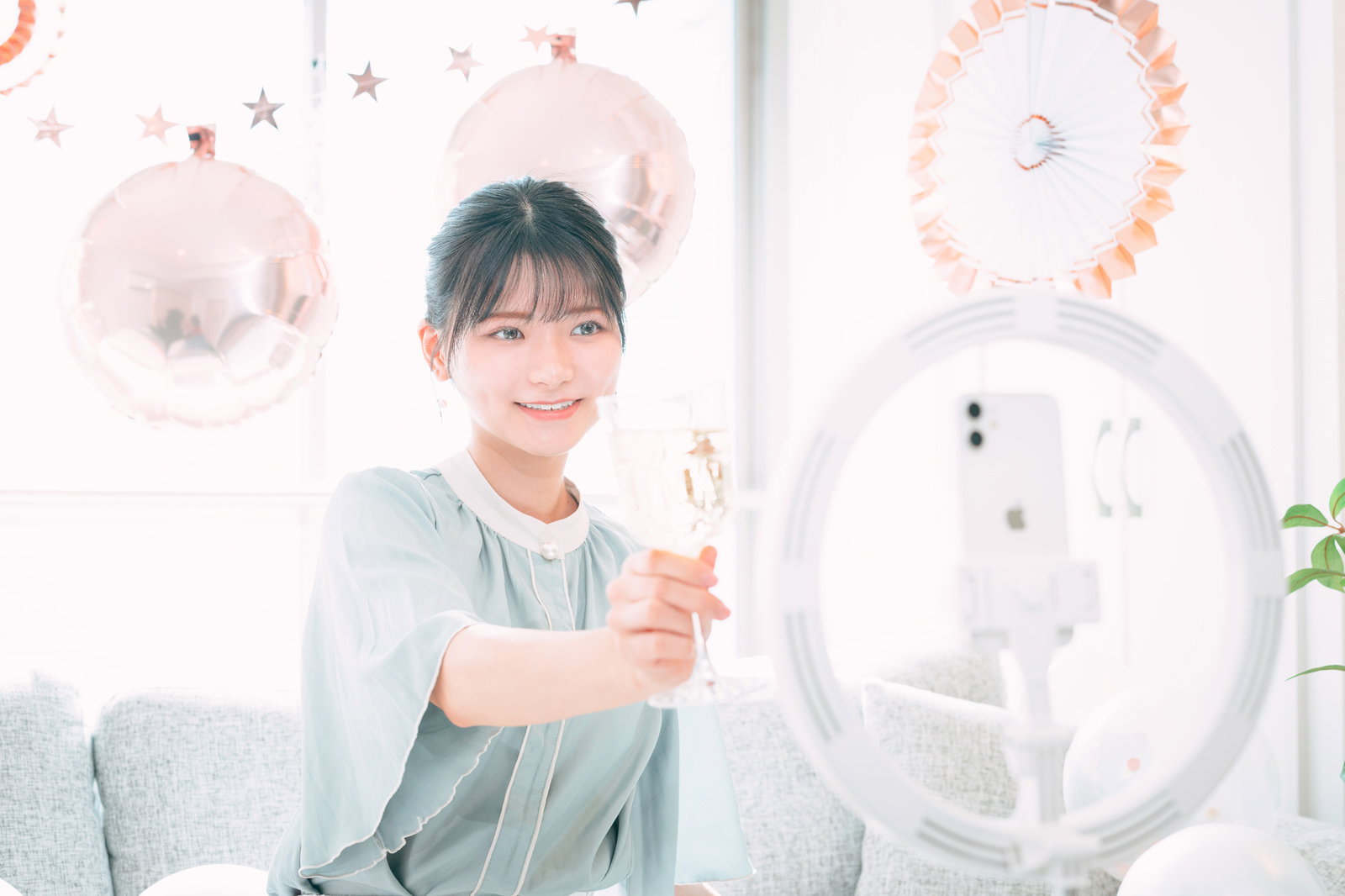 白い服を着た女性が室内でシャンパングラスを持ち笑顔で乾杯している様子［モデル：モデルリリース］