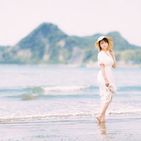 白いワンピース姿で波打ち際を歩く彼女の夏ポートレートの写真