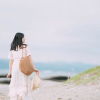 海岸沿いを散歩する麦わら帽子姿の女性の後ろ姿の写真