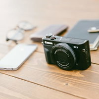 黒いコンパクトデジカメとスマホ、メモ帳が置かれた取材道具の写真