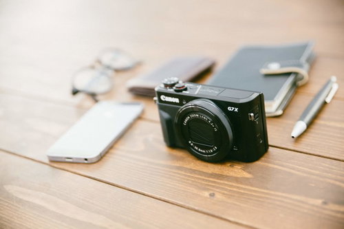 黒いコンパクトデジカメとスマホ、メモ帳が置かれた取材道具